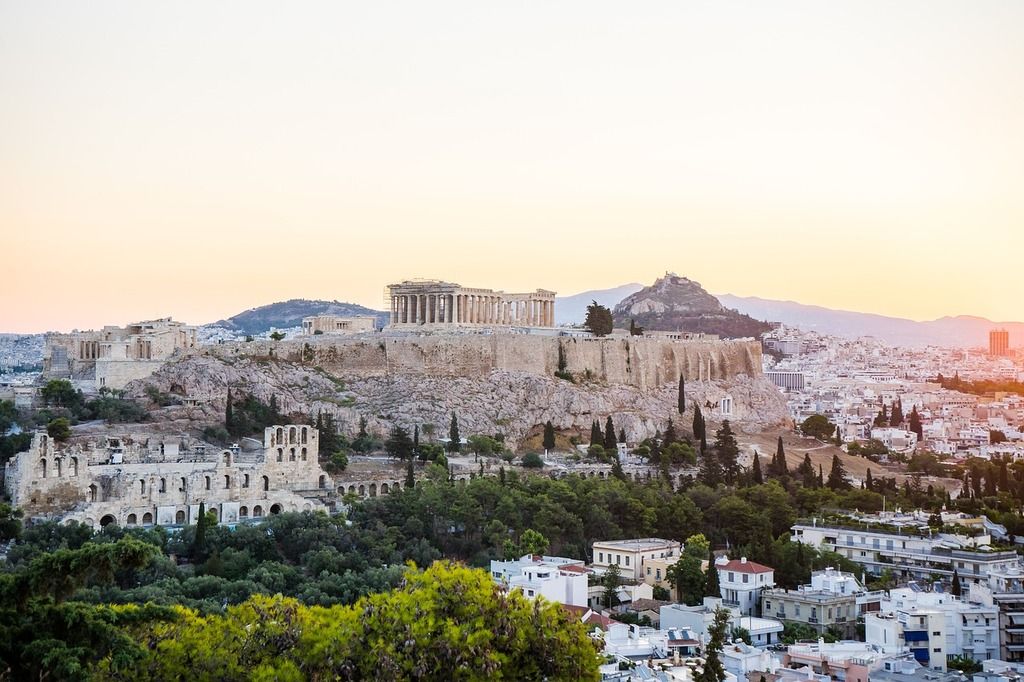 Vue panoramique de l'Acropole d'Athènes au coucher du soleil, avec le Parthénon dominant la colline et la ville en arrière-plan.