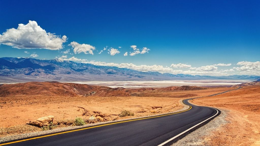 Route sinueuse traversant le désert de la Vallée de la Mort aux États-Unis, avec des montagnes et un ciel dégagé en arrière-plan.