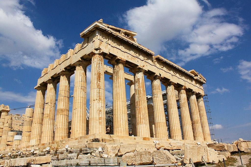 Gros plan sur le Parthénon d'Athènes, monument antique aux imposantes colonnes dorées sous un ciel bleu.