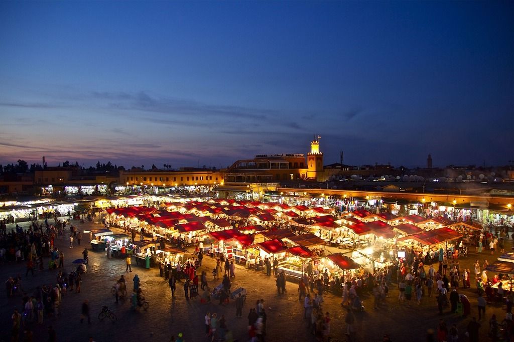 Vue nocturne animée de la place Jemaa el-Fna à Marrakech avec ses étals illuminés et son ambiance vibrante.