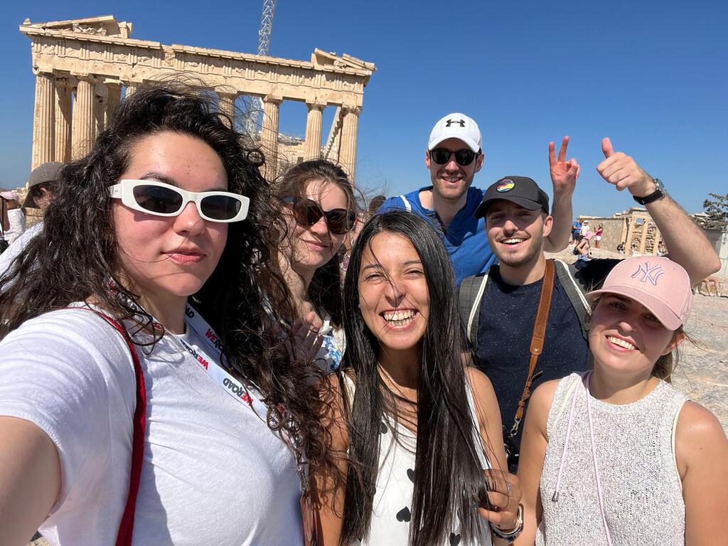 Un groupe de voyageurs souriant devant le Parthénon lors d’un voyage de groupe organisé à Athènes.