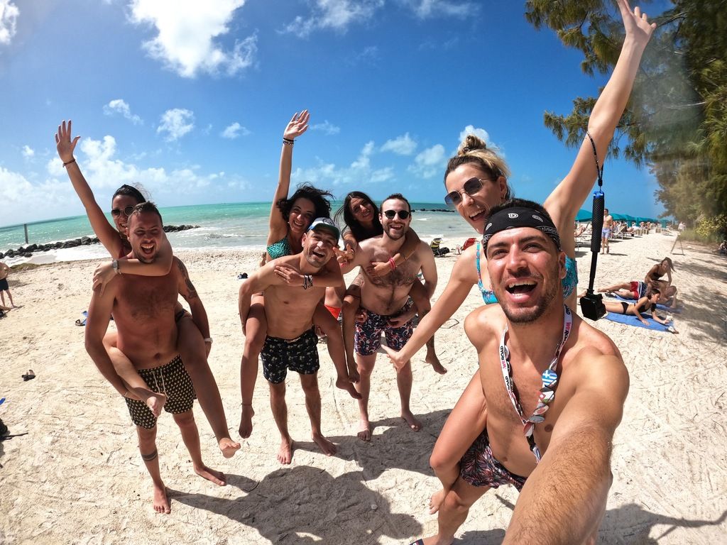 Groupe de voyageurs souriants sur une plage de sable blanc en Floride, lors d’un voyage de groupe organisé par WeRoad, avec une mer turquoise et un ciel bleu en arrière-plan