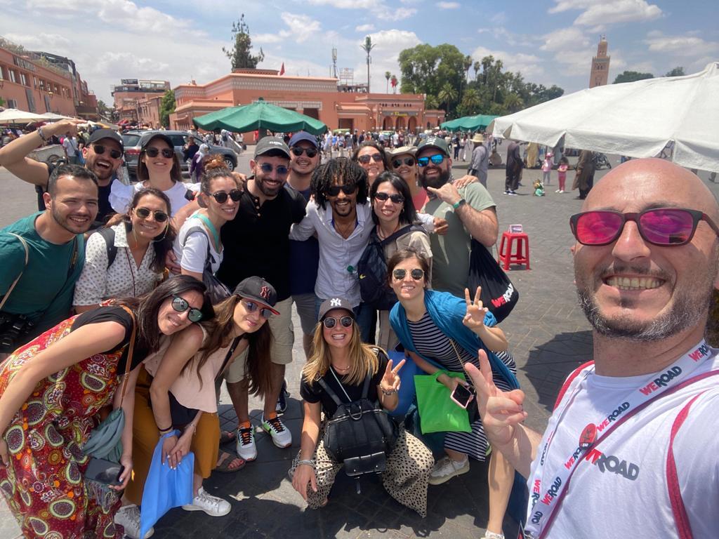 Un groupe de voyageurs souriants posant sur la place Jemaa el-Fna à Marrakech lors d’un voyage organisé par WeRoad.