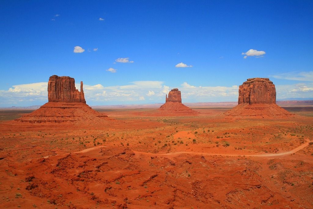 Paysage iconique de Monument Valley, avec ses formations rocheuses rouges sous un ciel bleu clair.