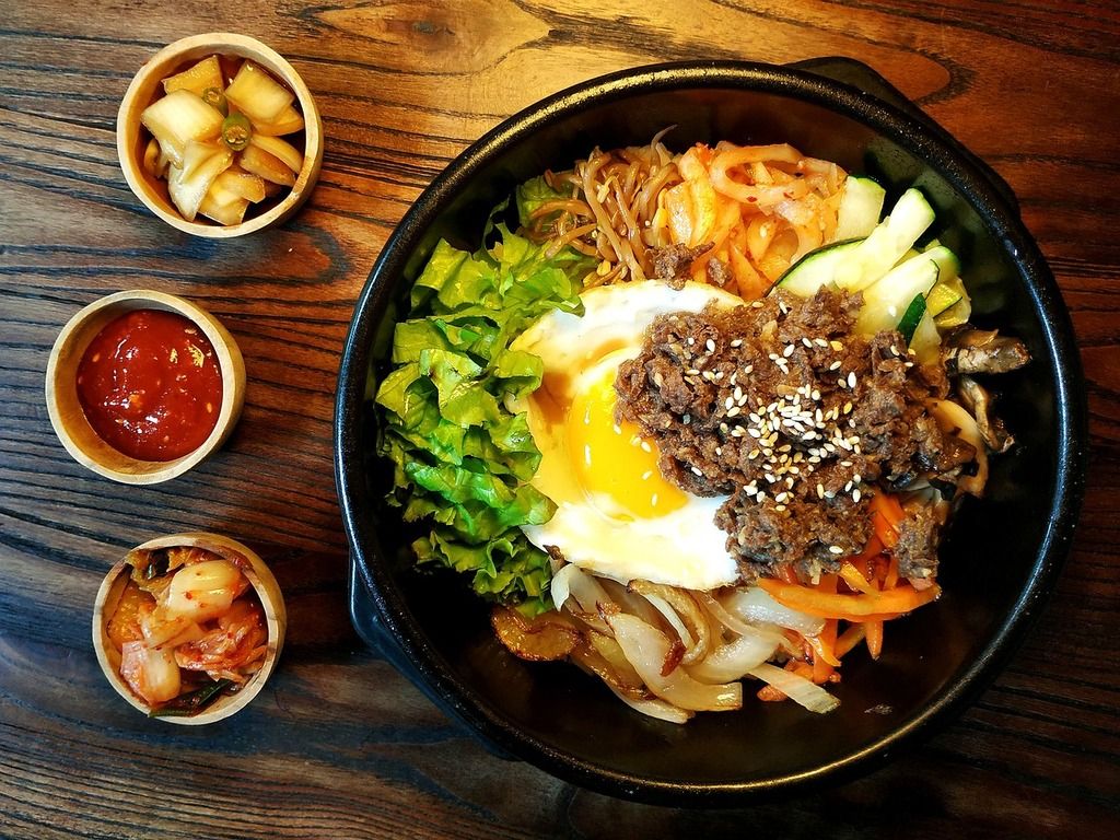 Un bol de bibimbap coréen avec du riz, des légumes, du bœuf mariné, un œuf au centre et du gochujang, accompagné de petits plats d'accompagnement.