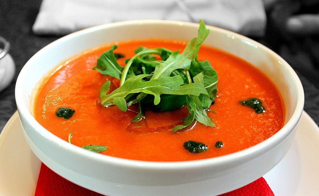 Soupe froide de gaspacho garnie de roquette fraîche dans un bol blanc.