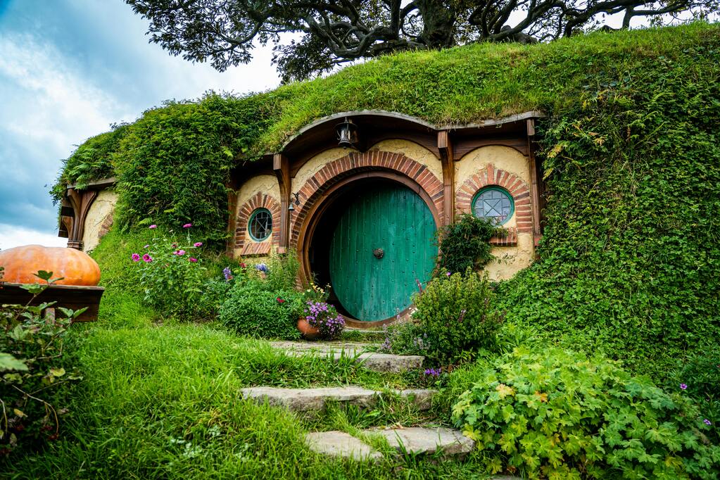 Une maison de Hobbiton en Nouvelle-Zélande, avec une porte ronde verte et un jardin luxuriant.