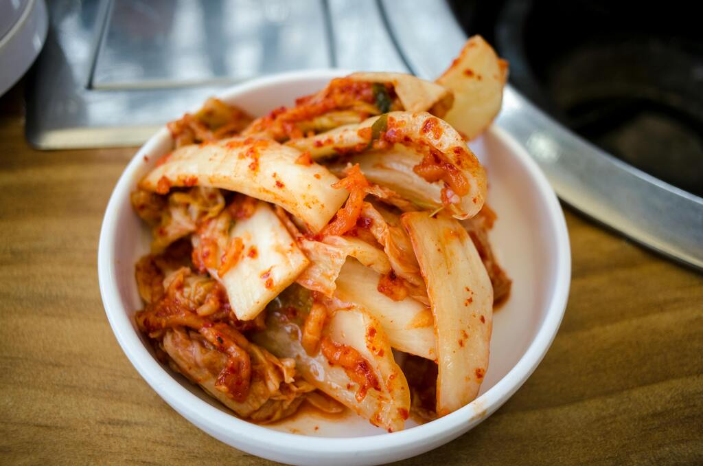 Un bol de kimchi épicé coréen servi dans un plat blanc sur une table en bois.