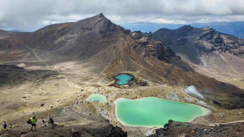 Paysage volcanique du Tongariro Alpine Crossing, avec les lacs d’émeraude et des randonneurs explorant la région.