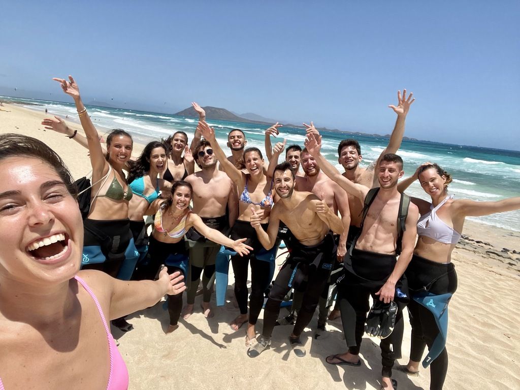 Voyage de groupe WeRoad sur la plage de Fuerteventura avec participants souriants en combinaisons de plongée