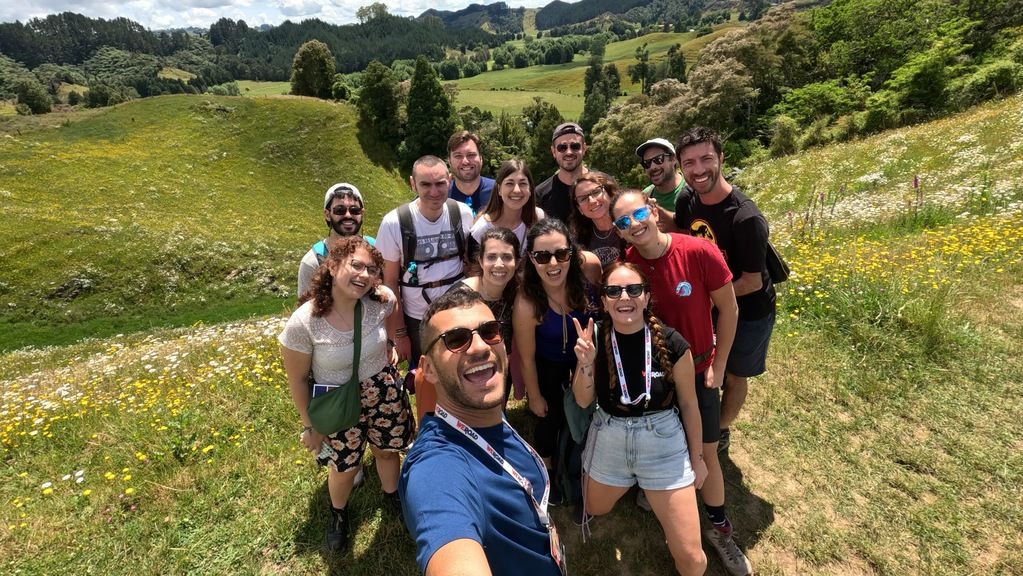 Un groupe de voyageurs WeRoad en Nouvelle-Zélande posant pour une photo dans une prairie verdoyante entourée de collines.