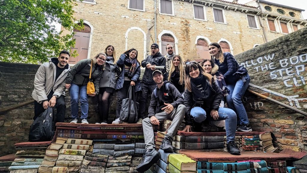 Groupe de voyageurs WeRoad à Strasbourg posant sur des marches couvertes de livres, capturant un moment de convivialité et d'exploration.