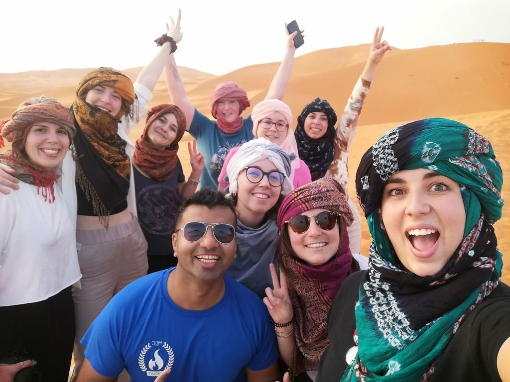 Groupe WeRoad en excursion dans le désert du Maroc, un voyage inoubliable à travers les dunes de sable doré avec des foulards traditionnels.