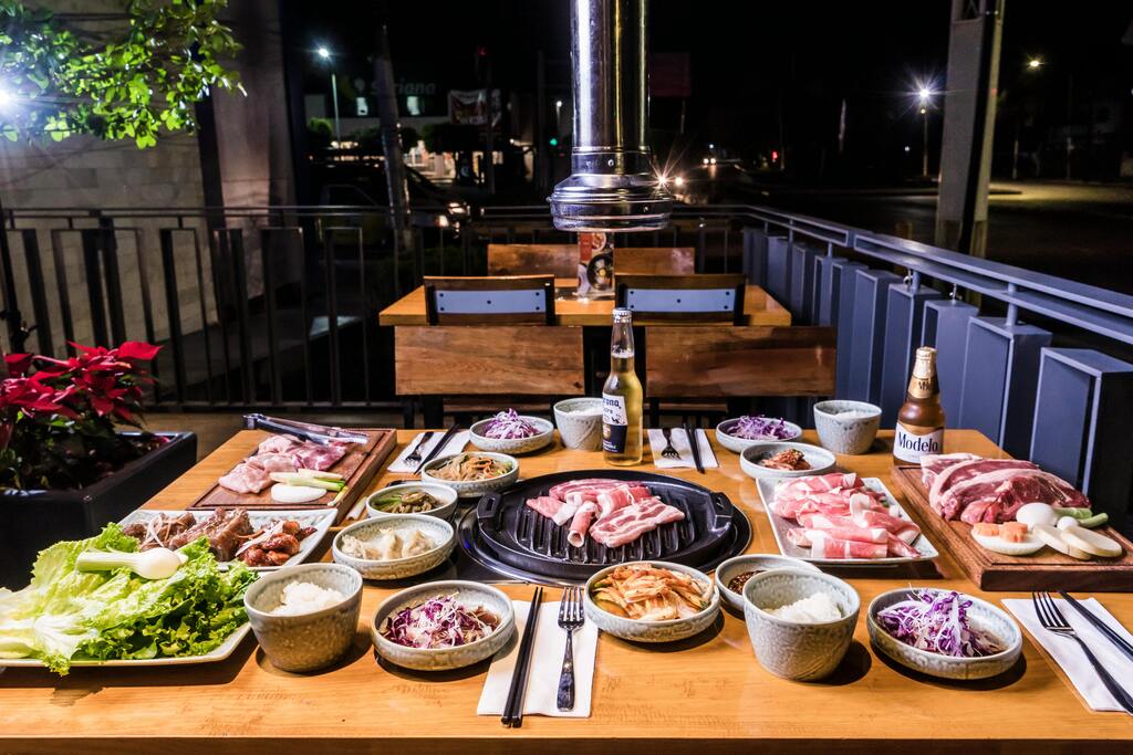 Un barbecue coréen en plein air avec une table remplie de viandes marinées, de légumes, de kimchi et de divers accompagnements.