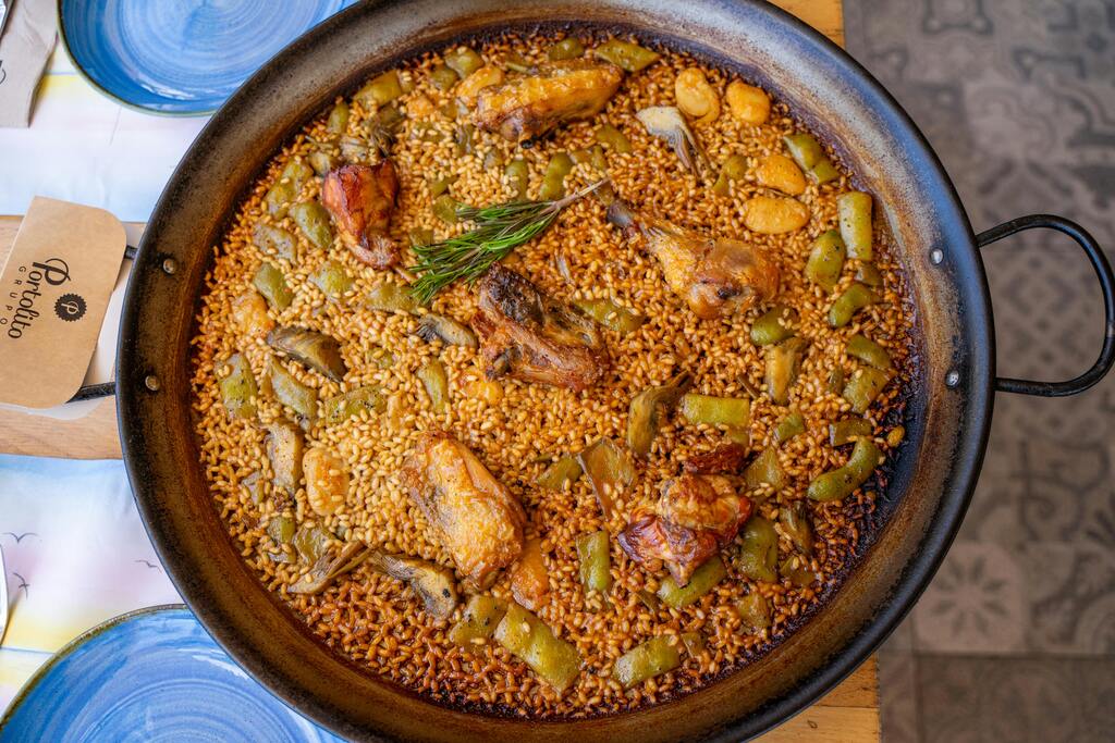 Paella traditionnelle avec poulet, légumes verts et riz, servie dans une poêle en fonte.