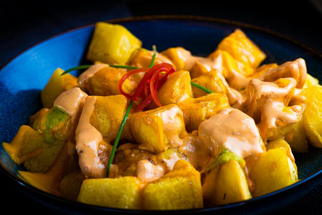 Plat de pommes de terre épicées avec une sauce crémeuse, servi dans une assiette bleue.