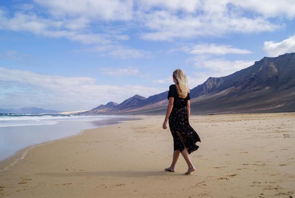 Femme marchant seule sur une plage déserte avec des montagnes en arrière-plan à Fuerteventura