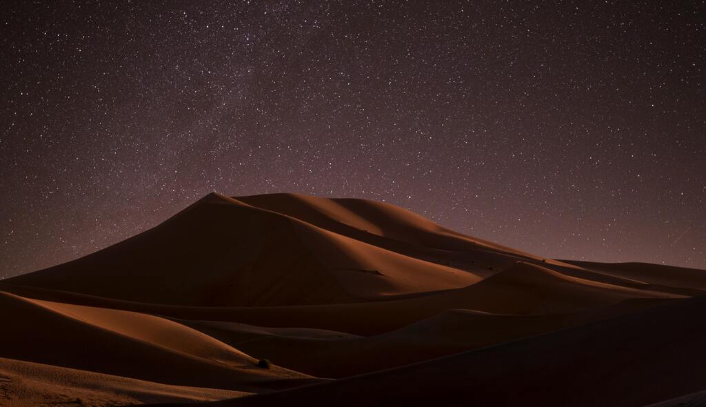 Une vue époustouflante des dunes de sable illuminées par la lumière des étoiles dans le désert.