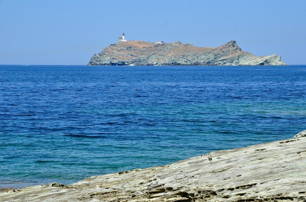 Phare sur une île rocheuse entourée d'une mer bleu profond, vue depuis le rivage en Corse.