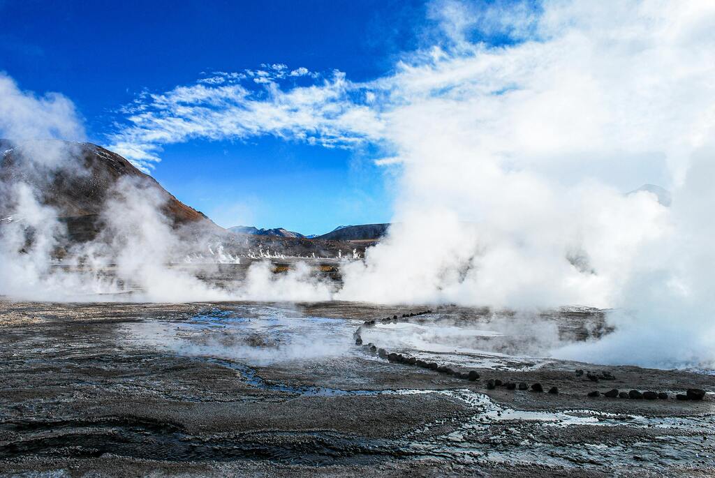 Geysers del Tatio, Chili, avec des colonnes de vapeur s'élevant dans un paysage volcanique sous un ciel bleu.