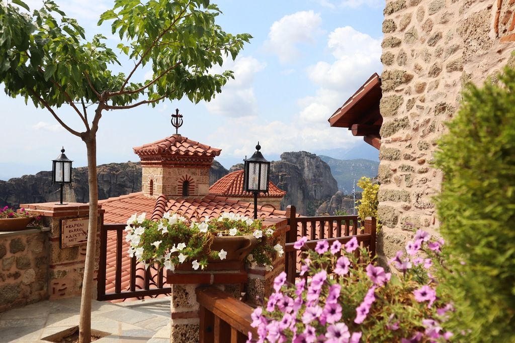 Vue sur un monastère des Météores en Grèce avec des fleurs et des montagnes en arrière-plan.