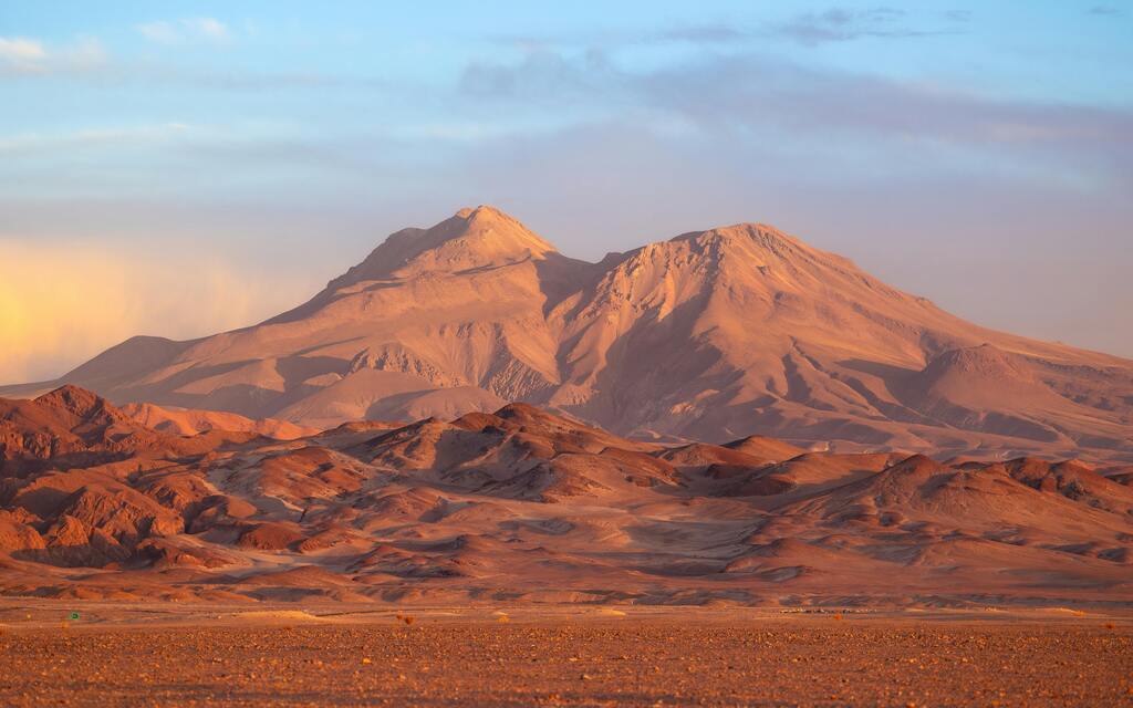 Montagnes du désert d'Atacama sous la lumière du coucher du soleil, avec des teintes rouges et orangées.