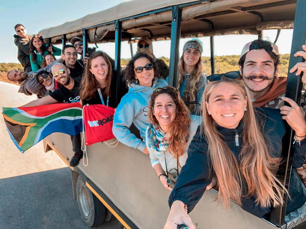 Un groupe de voyageurs enthousiastes profitant d’un safari, brandissant un drapeau sud-africain et un drapeau WeRoad.