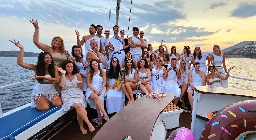 Un groupe de voyageurs WeRoad en Grèce, vêtus de blanc, profitant d'une croisière au coucher du soleil.