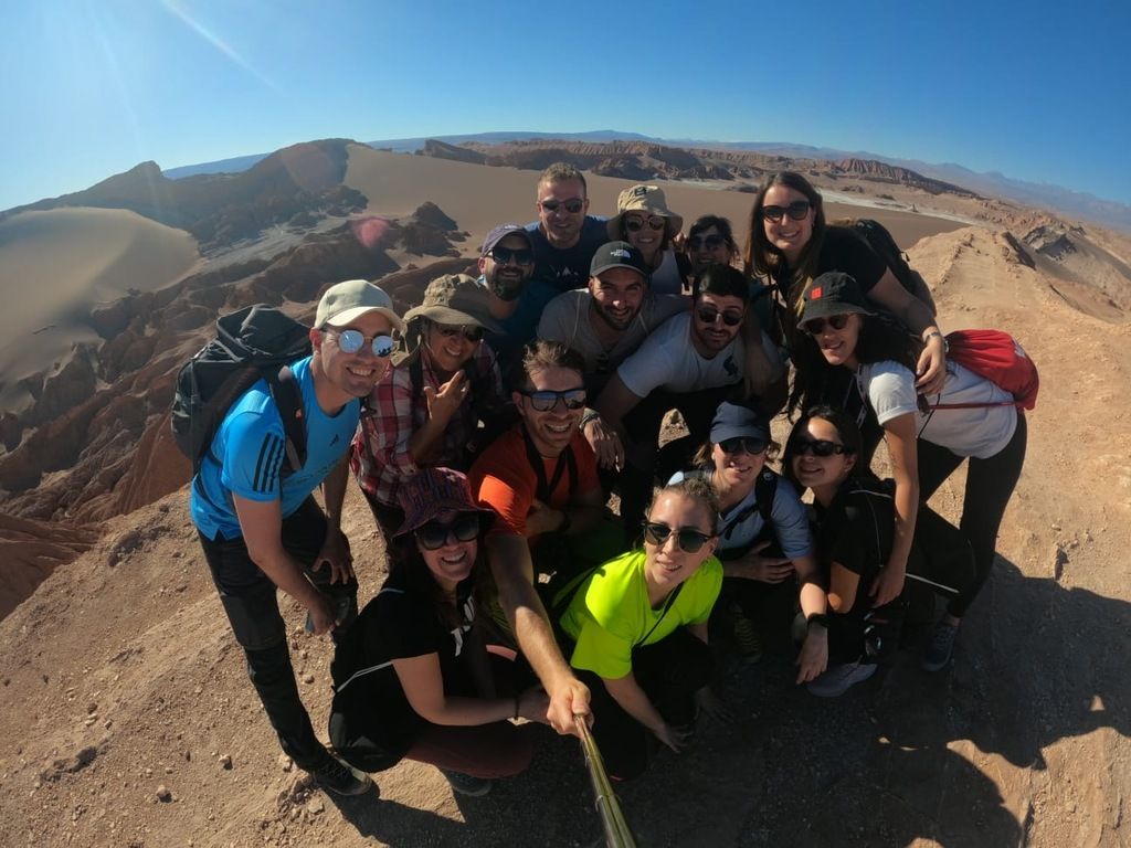 Voyage de groupe WeRoad dans le désert d'Atacama, avec des voyageurs souriants prenant une photo de groupe sur une colline rocheuse.