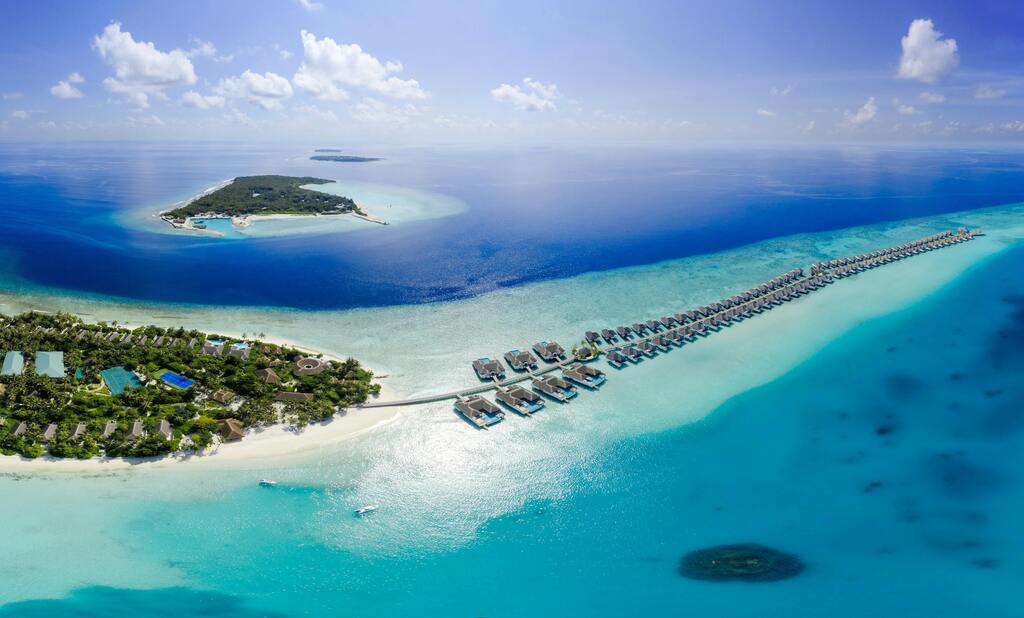 Vue aérienne d'une île tropicale avec des villas sur pilotis et des eaux turquoise aux Maldives.