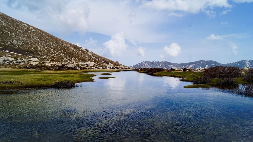 Lac de montagne aux eaux cristallines, entouré de collines et d’un ciel nuageux en Corse.