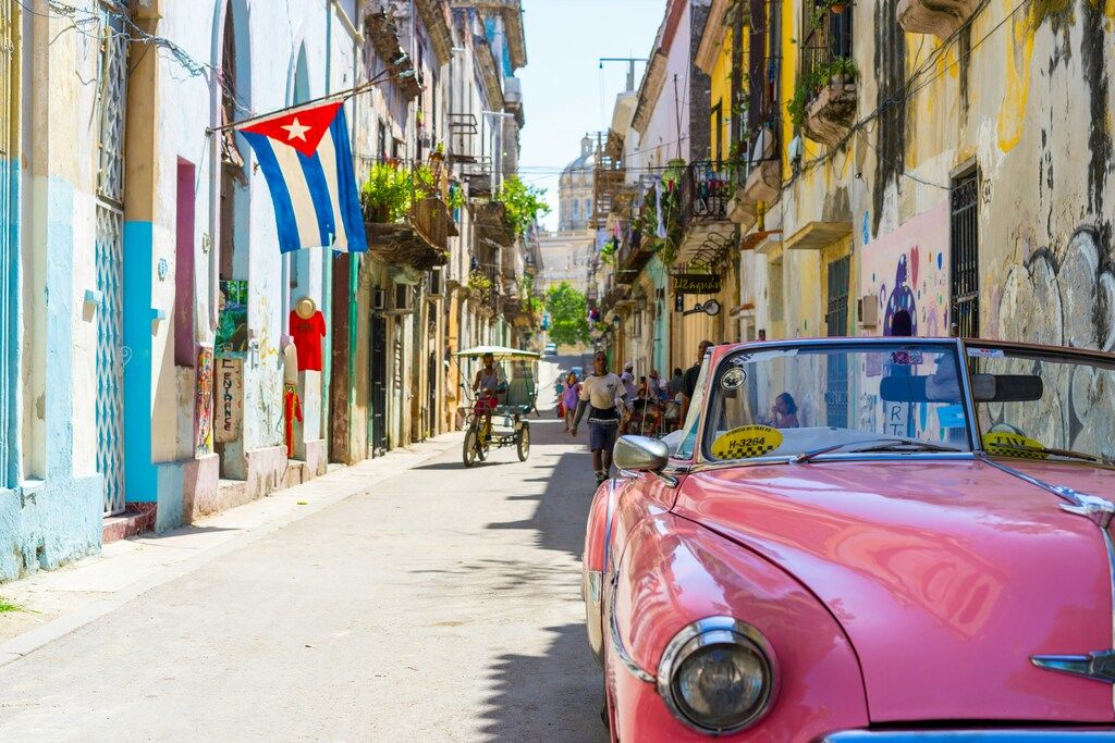 Rue animée de La Havane, Cuba, avec une voiture rose et un drapeau cubain.