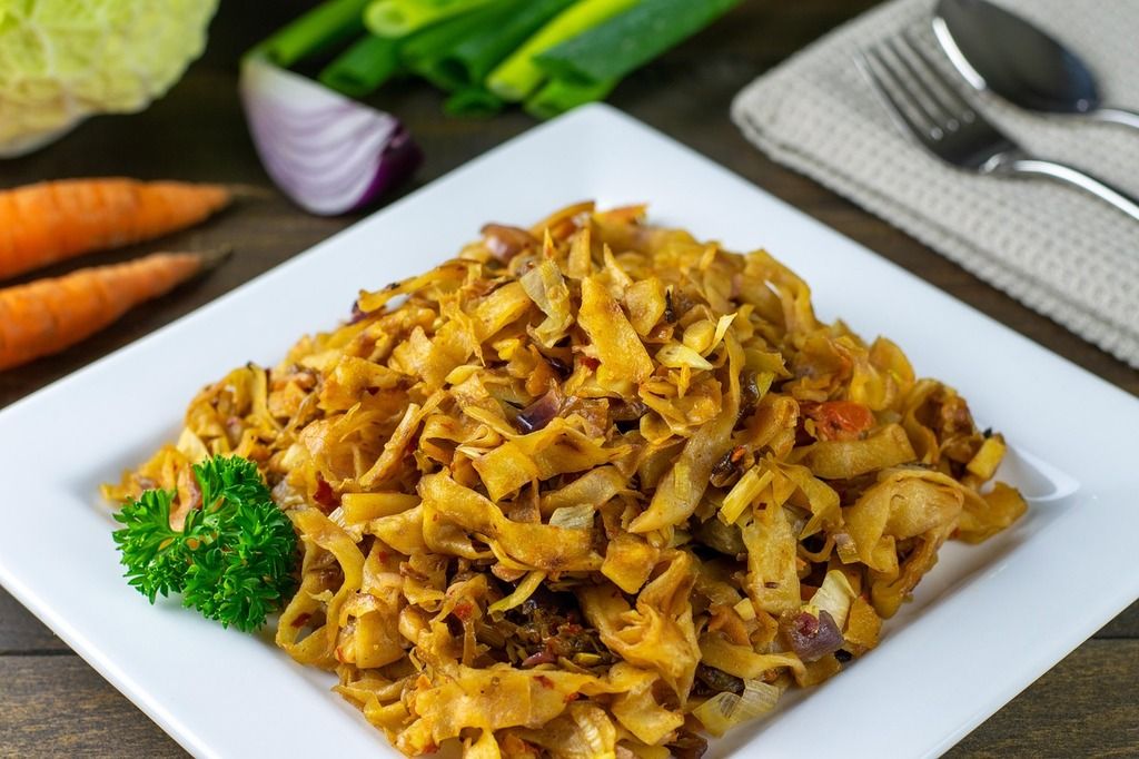 Assiette de kottu roti, plat sri lankais à base de pain plat haché, légumes sautés et épices, servie sur une assiette carrée blanche.