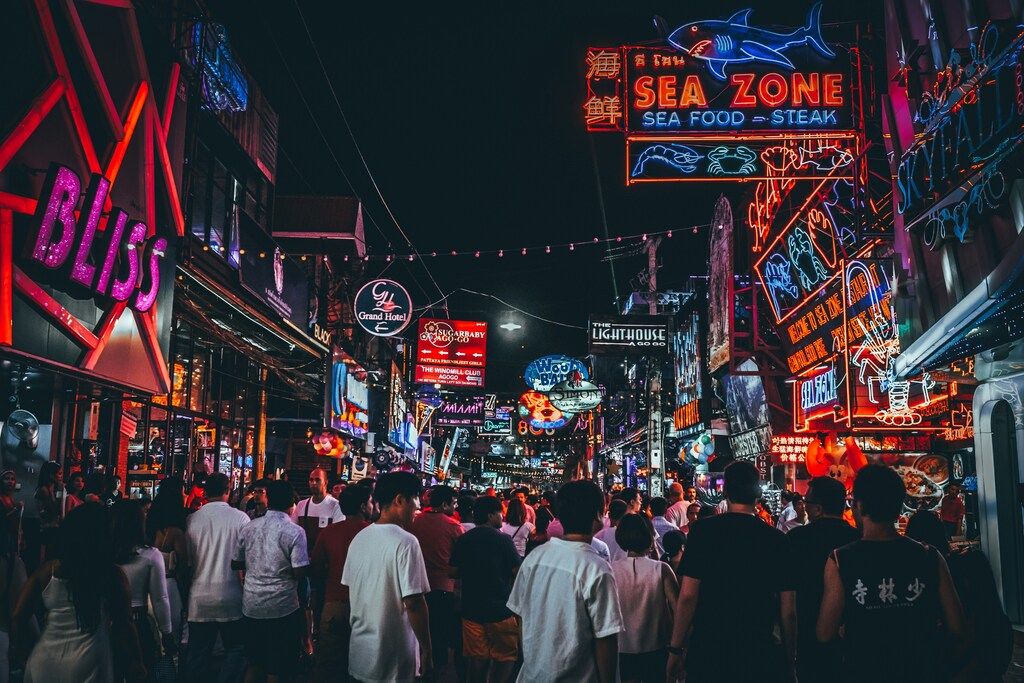 Rue de ville animée la nuit, illuminée par des néons colorés.