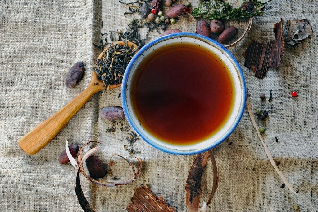 Tasse de thé noir vue de dessus, entourée de feuilles de thé séchées, épices et cacao, sur un tissu en lin naturel.