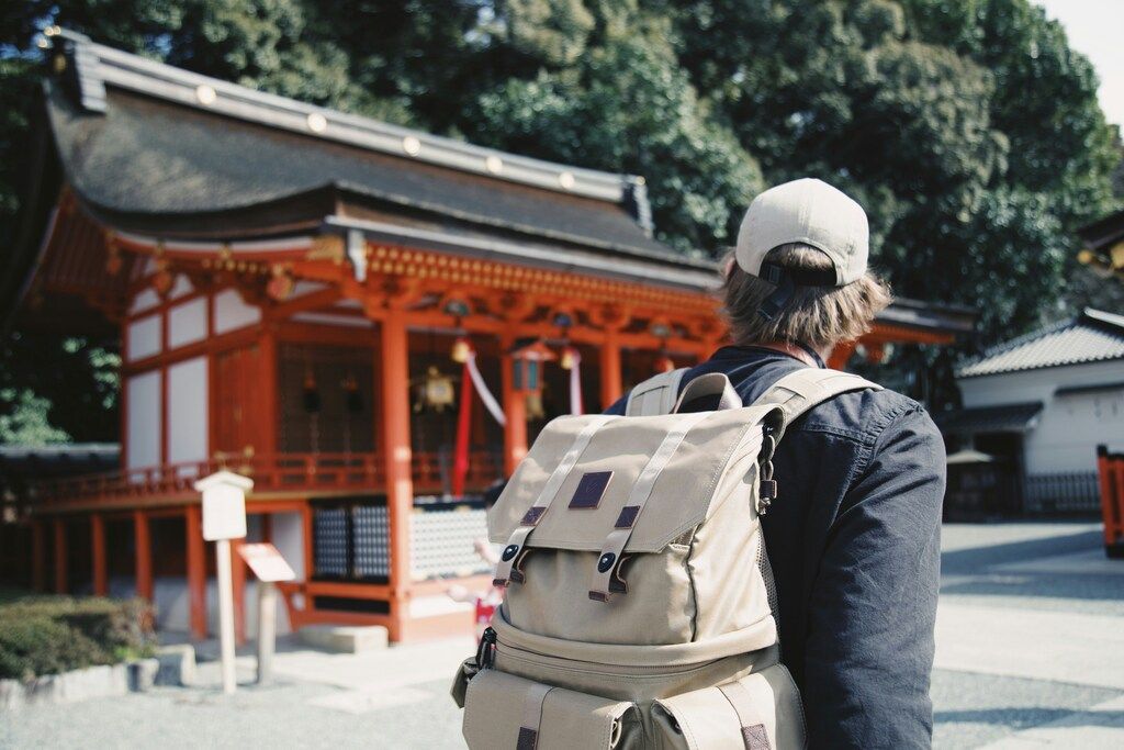 Voyageur avec un sac à dos face à un sanctuaire traditionnel en bois rouge au Japon.