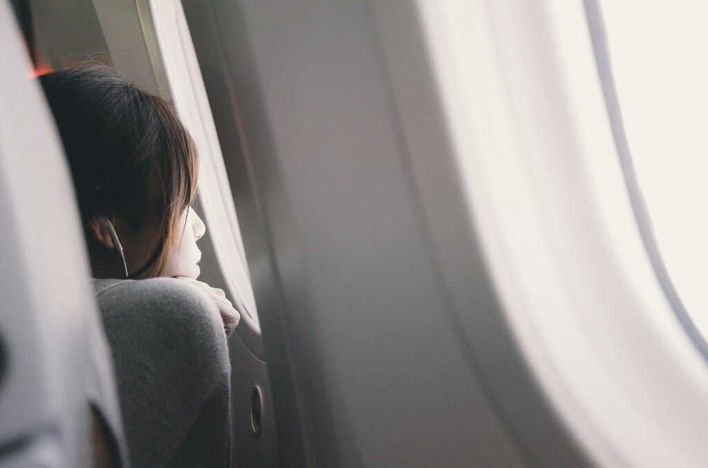 Jeune femme regardant par le hublot d’un avion pendant un vol, avec écouteurs et lumière naturelle douce