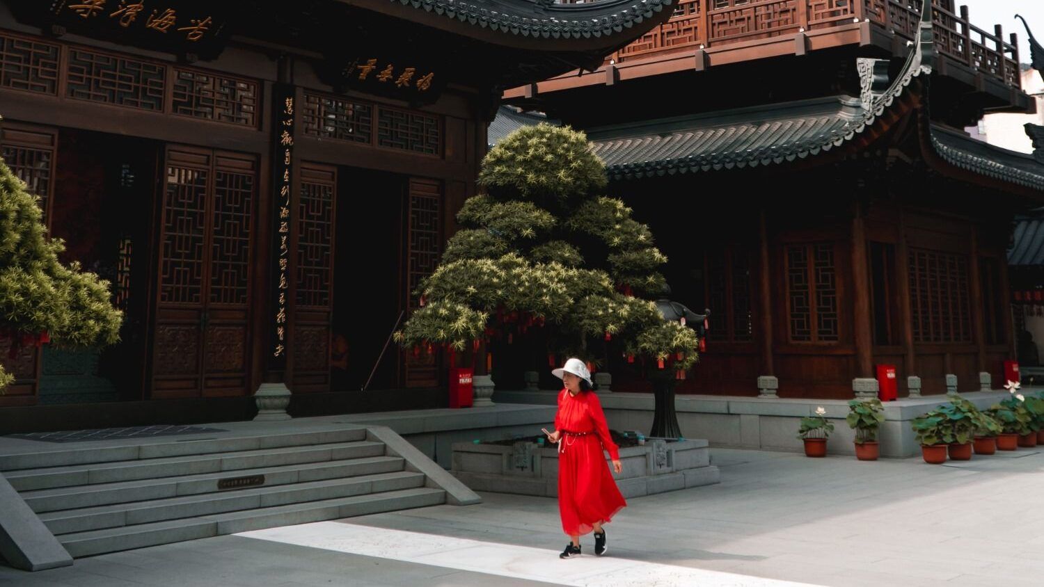 Femme en rouge marchant dans la cour d'un temple chinois traditionnel.