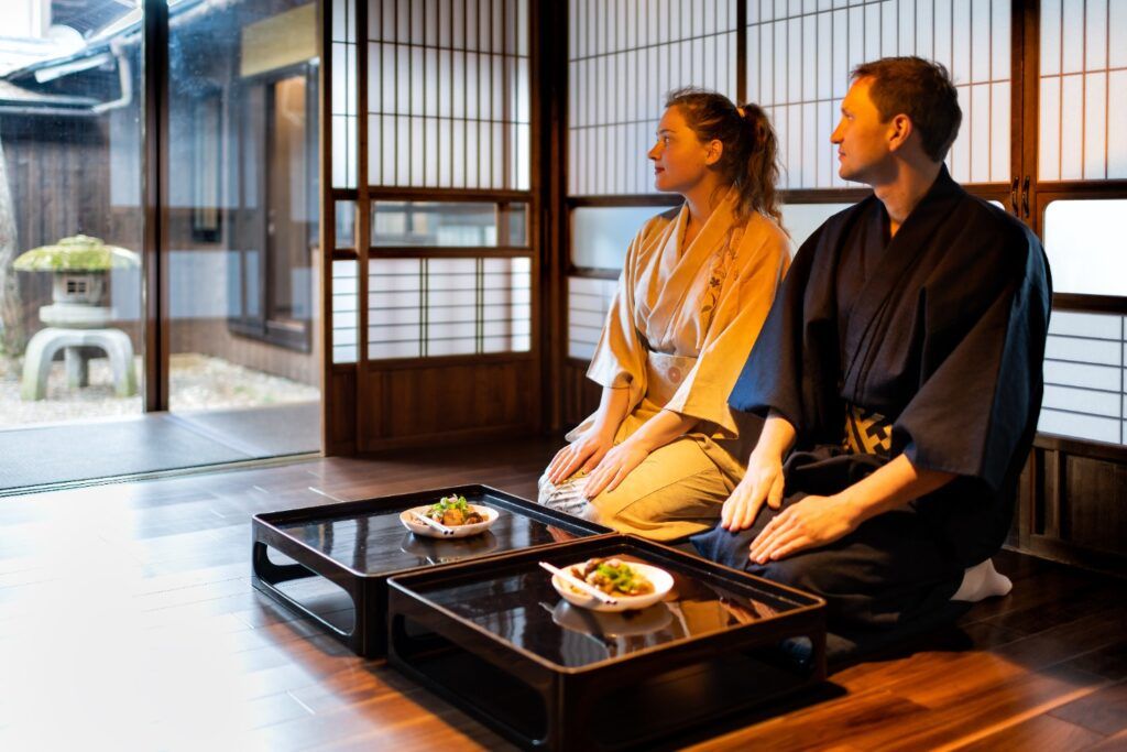 Un couple en kimono, assis en seiza sur le sol d'un ryokan (auberge traditionnelle), devant des petites tables de repas.