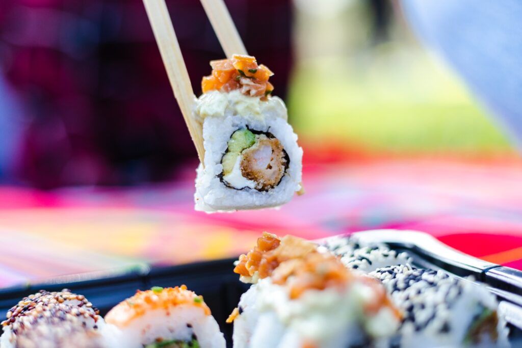 Gros plan sur un rouleau de maki de style Nikkei (crevette tempura et avocat) tenu par des baguettes.