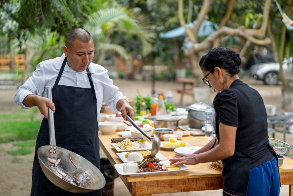 Chef préparant un plat sauté de Lomo Saltado en plein air, le dressant dans l'assiette.