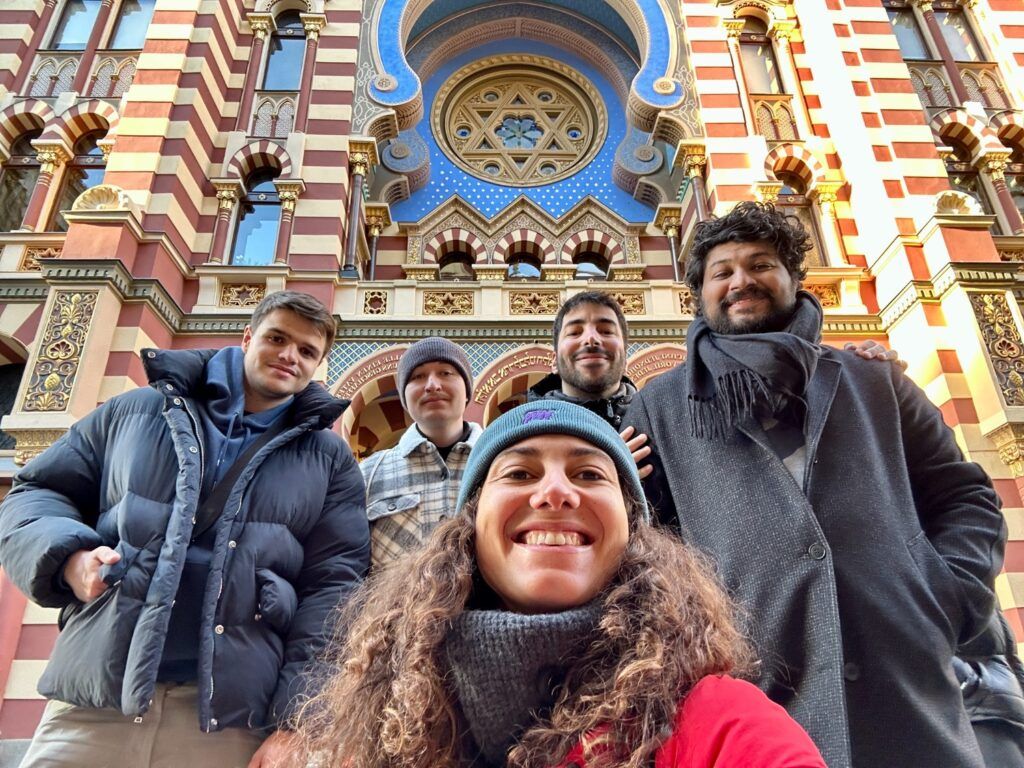 Groupe de voyageurs WeRoad souriants devant une synagogue colorée à Prague.