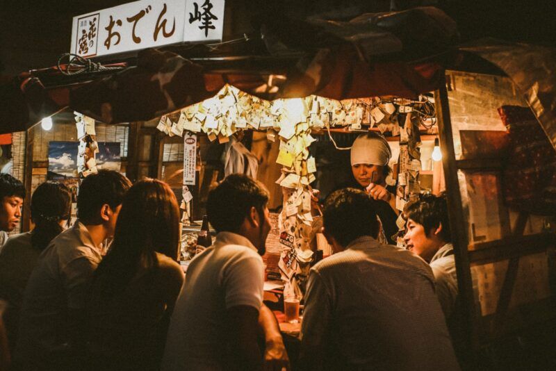 Stand de yatai traditionnel japonais, éclairé la nuit, où des clients sont assis au comptoir et discutent avec le chef sous une enseigne d'Oden. Stand de yatai traditionnel japonais, éclairé la nuit, où des clients sont assis au comptoir et discutent avec le chef sous une enseigne d'Oden.