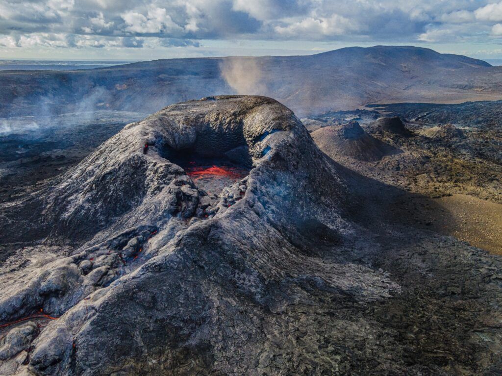 Cratère d'un volcan actif dans la péninsule de Reykjanes en Islande, avec de la lave rougeoyante visible et de la fumée s'échappant du cône.
