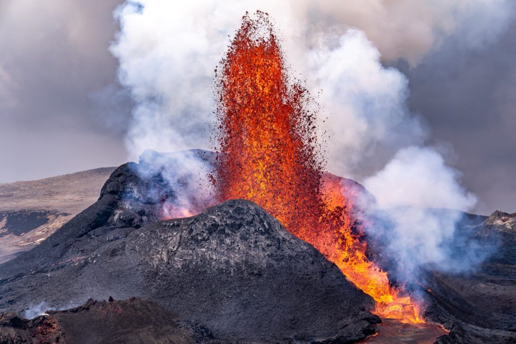 Fontaine de lave en éruption au volcan Fagradalsfjall en Islande, montrant des projections de roche en fusion et de la fumée s'échappant du cône.