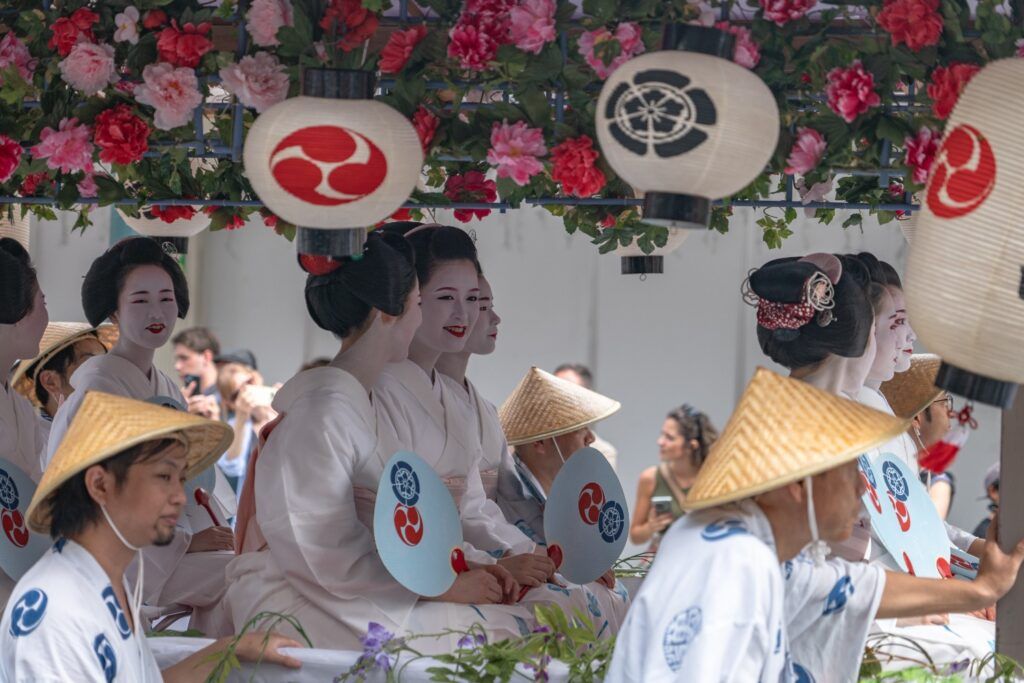Scène de festival japonais : femmes en kimonos blancs et maquillage Geisha sur un char décoré de lanternes et de fleurs roses et rouges.