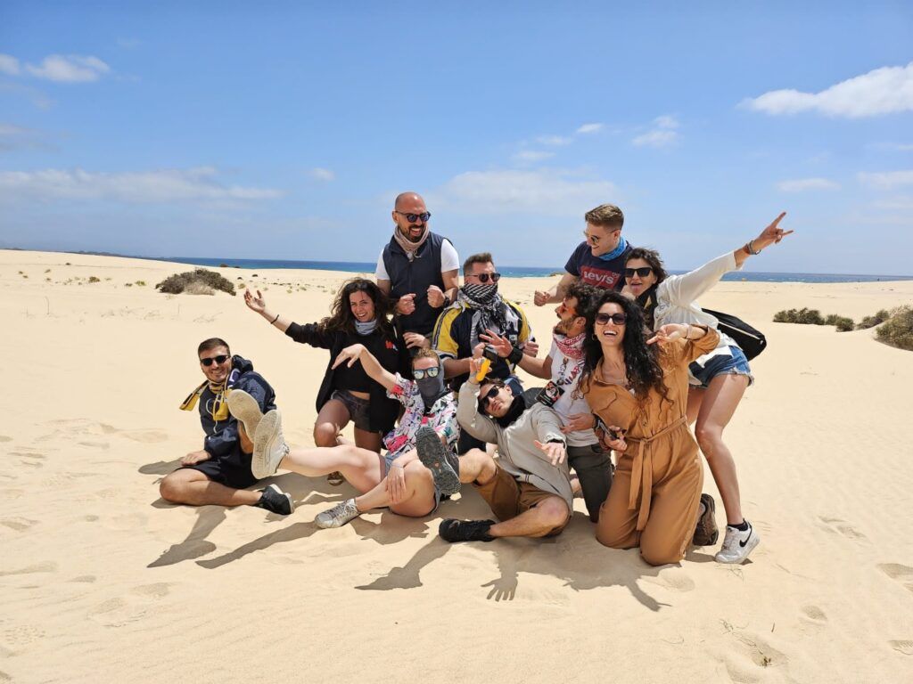 Un groupe de voyageurs WeRoad joyeux pose sur les dunes de sable d'une plage égyptienne sous un ciel bleu.