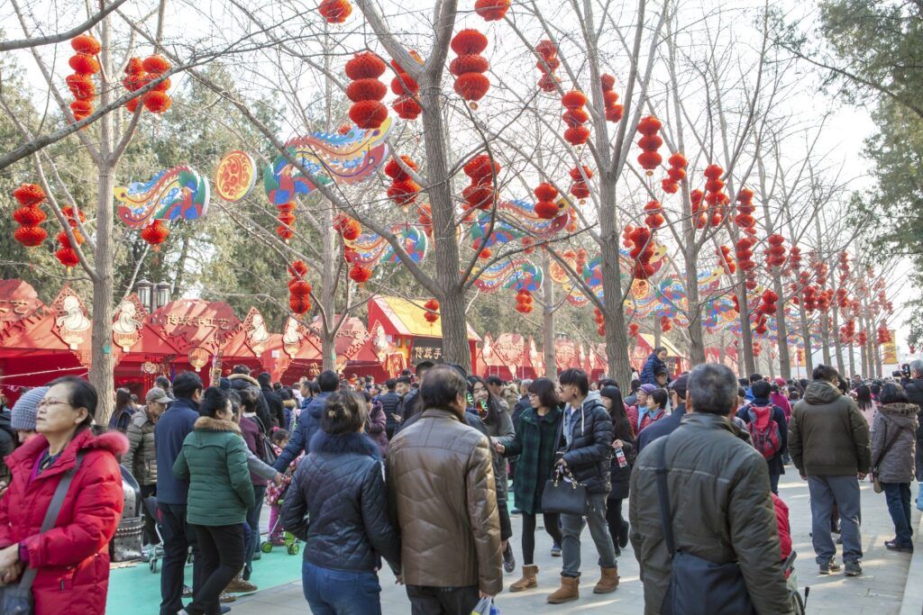 Une foule de personnes célèbre le Nouvel An chinois à Pékin, marchant sous des arbres décorés de lanternes rouges traditionnelles et de décorations colorées.